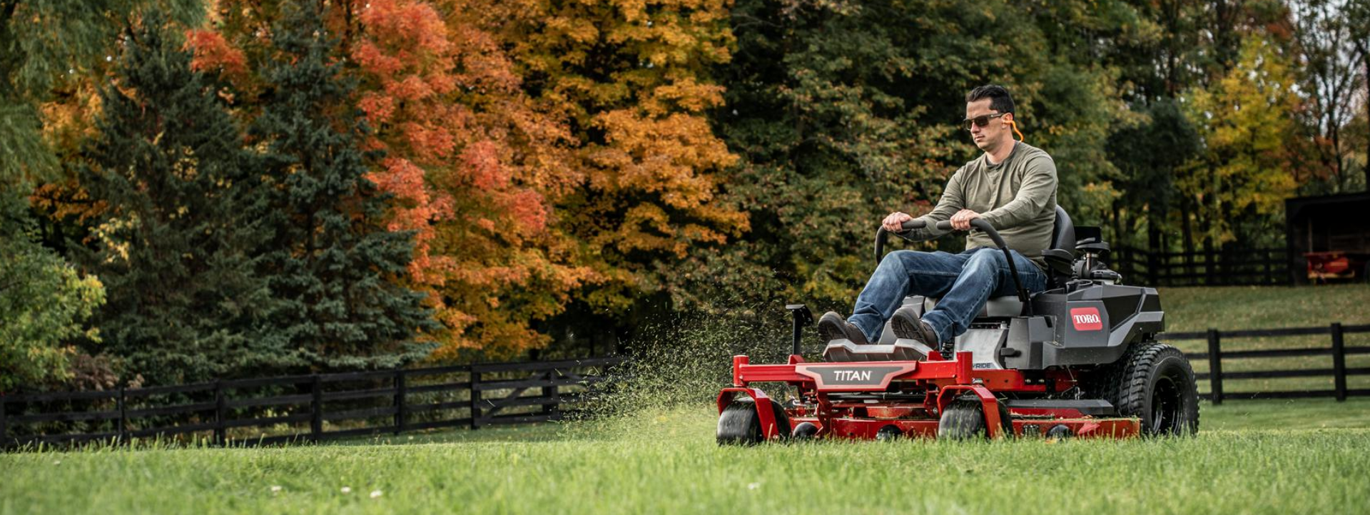 Image of man on Toro zero turn mower, mowing lawn in front of a fence