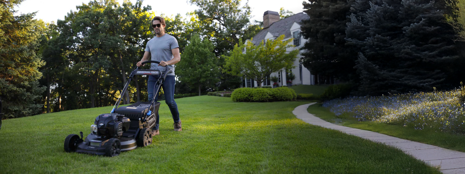 Man using a Toro Super Recycler mower in a front yard by a concrete walkway. Built to Last. Proven to Perform.