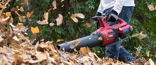 image shows a man leaf blowing a pile of leaves with a 60V battery leaf blower